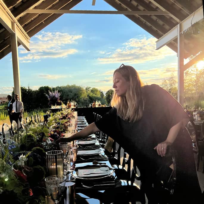 A long table at sunset ready for a wedding reception. Carrie Sartor leaning over making a final adjustment.